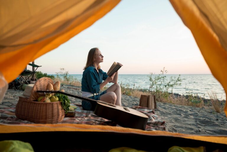 Woman reading a book at a beach campsite at sunset, seen from inside a tent, camping in Musandam